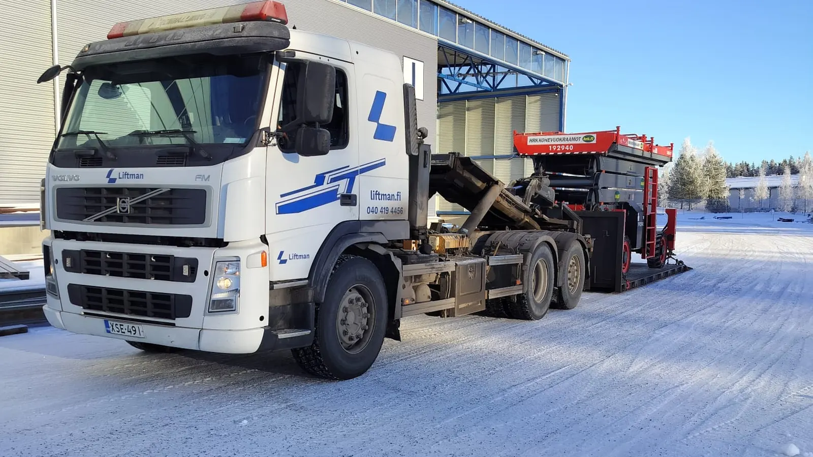 Liftmanin valkoinen Volvo-vaihtolava-auto ja saksilava kuljetuksessa talvisella piha-alueella