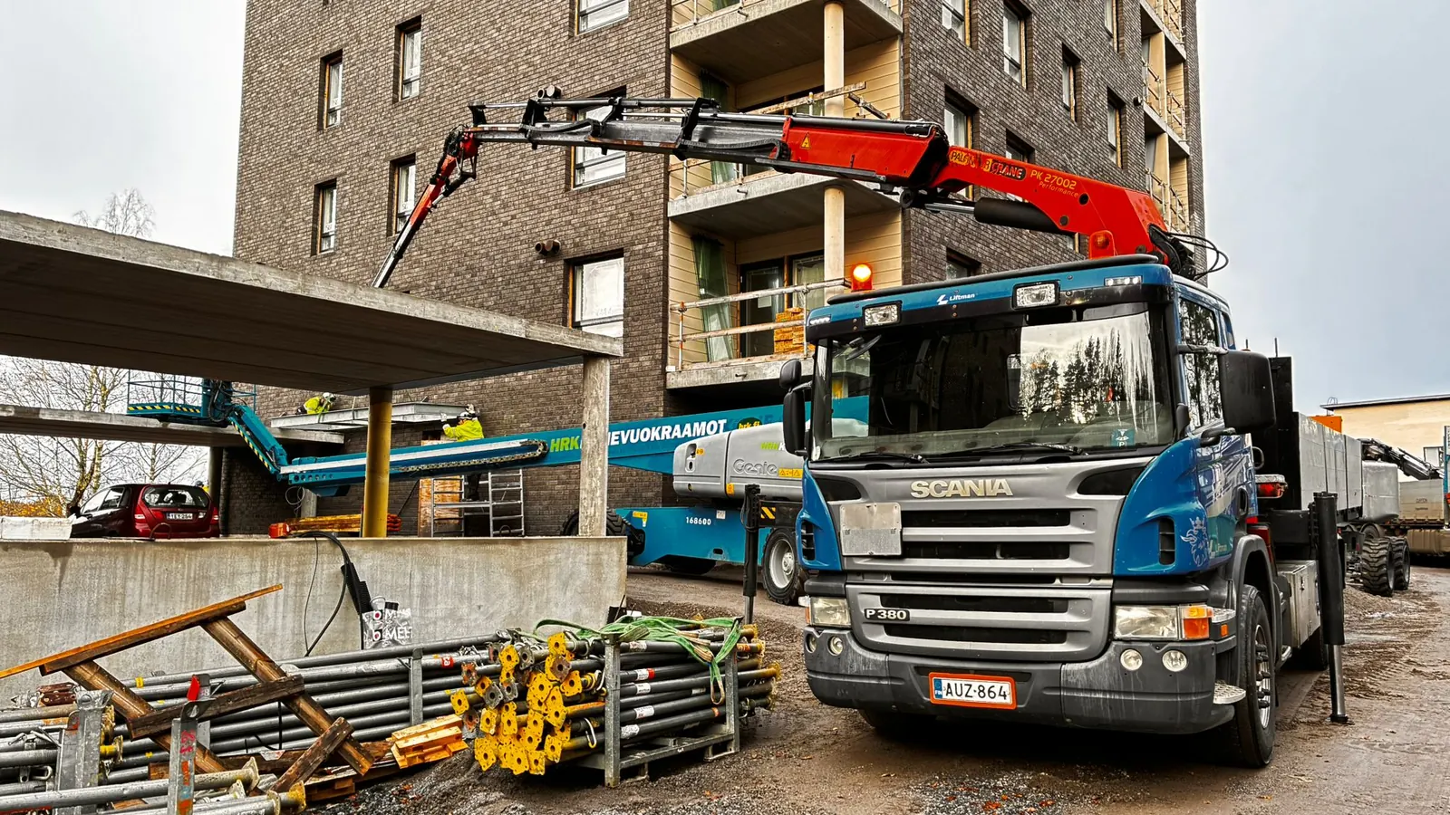 Liftmanin sininen Scania-nosturiauto nostaa rakennusmateriaalia kerrostalotyömaalla